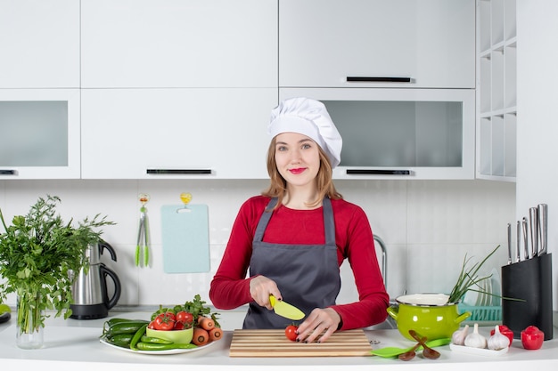 Cuoca sorridente di vista frontale in grembiule che taglia pomodoro a pezzi