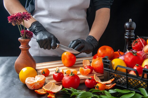 Cuoca vista frontale che taglia mandarini su insalata di cottura scura dieta salute pasto vegetale cibo frutta lavoro
