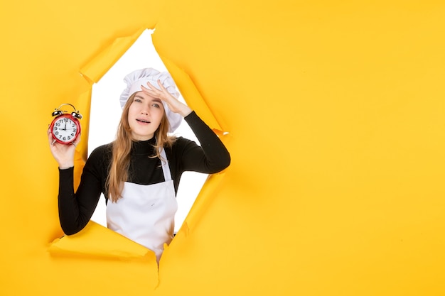 Cuoca vista frontale che tiene gli orologi sul tempo giallo cibo foto lavoro cucina emozione colore del sole