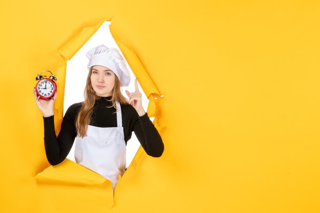 Cuoca vista frontale che tiene gli orologi sul tempo giallo foto cibo cucina emozione cucina sole colore