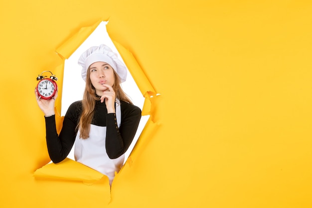 Cuoca vista frontale che tiene gli orologi sul tempo giallo foto lavoro cucina emozione cucina sole colore