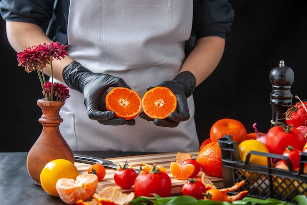 Cuoca vista frontale che tiene i mandarini tagliati a metà su insalata di cottura scura salute pasto vegetale cibo frutta dieta lavoro