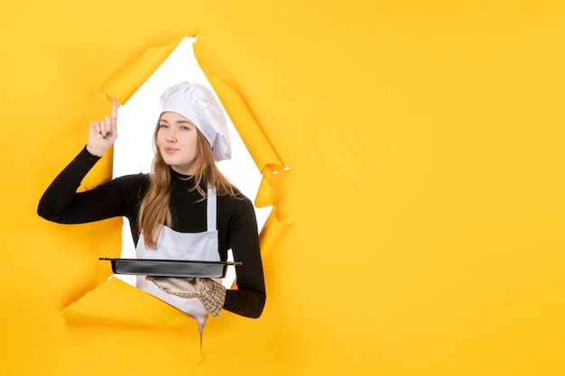 Cuoca vista frontale che tiene in mano una padella nera su giallo emozione cibo foto lavoro cucina cucina colore