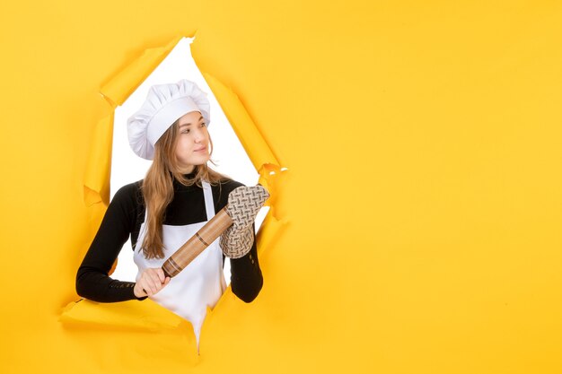 Cuoca vista frontale che tiene mattarello sulla foto gialla cucina lavoro colore cibo sole