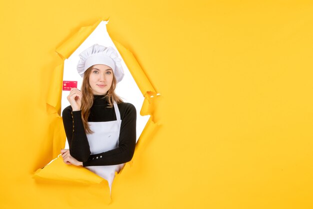 Cuoca vista frontale che tiene una carta bancaria rossa su soldi gialli colore lavoro foto cibo cucina cucina emozioni