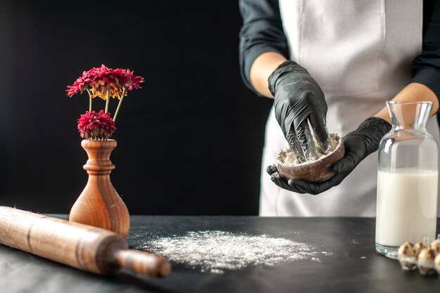 Cuoca vista frontale che versa farina bianca sul tavolo per l'impasto su frutta scura lavoro pasticceria torta torta cottura da forno