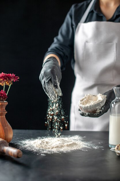 Cuoca vista frontale che versa farina bianca sul tavolo per l'impasto su un lavoro scuro torta di pasticceria panetteria cottura pasta cuocere la torta