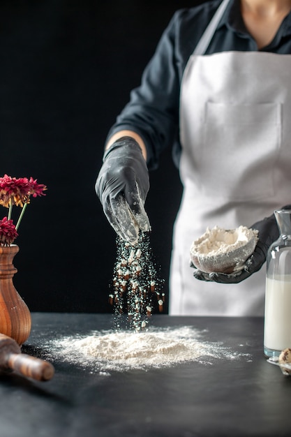 Cuoca vista frontale che versa farina bianca sul tavolo per l'impasto su un lavoro scuro torta di pasticceria panetteria cottura pasta cuocere la torta