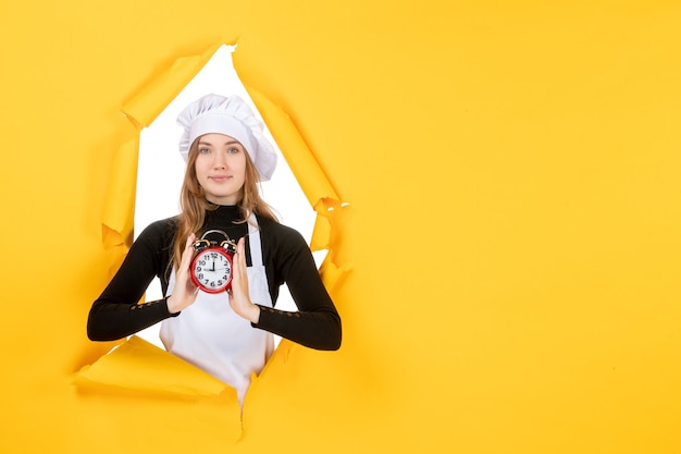 Cuoca vista frontale in berretto bianco cuoco con orologio su foto gialla colori lavoro cucina cucina cibo sole emozione