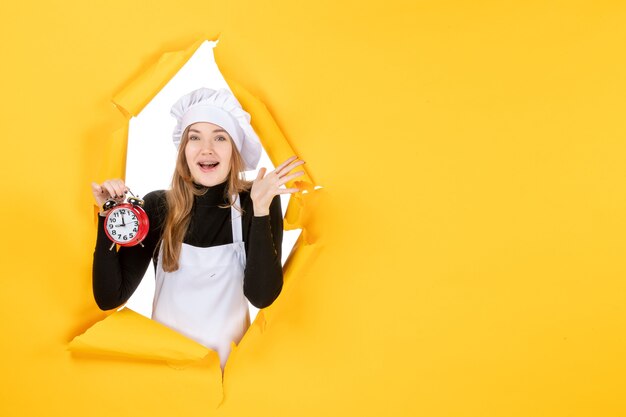 Cuoca vista frontale in berretto bianco cuoco con orologio su foto gialla lavoro cucina cucina cibo emozione