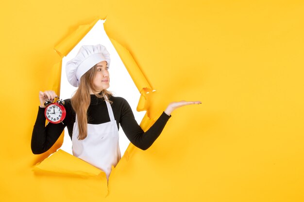 Cuoca vista frontale in berretto bianco da cuoco che tiene orologio su foto gialla lavoro a colori emozione cucina cucina cibo