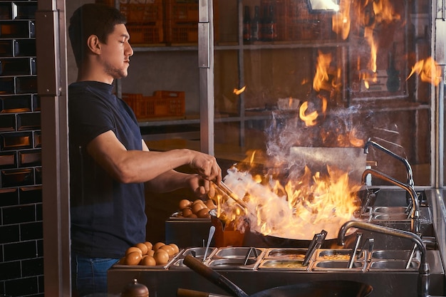 Cuocere è friggere le verdure con le spezie e la salsa in un wok su una fiamma. Processo di cottura in un ristorante asiatico.