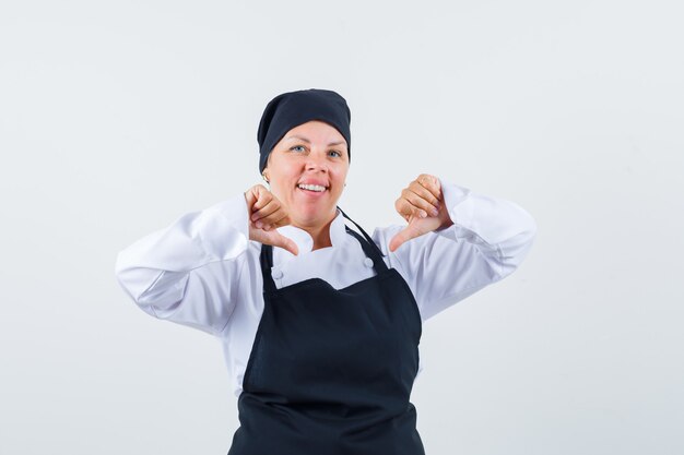 Cuoco femminile che indica a se stessa con i pollici in uniforme, grembiule e guardando fiero, vista frontale.