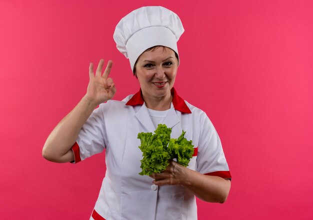 Cuoco femminile di mezza età sorridente in insalata uniforme della tenuta del cuoco unico che mostra il gesto okey