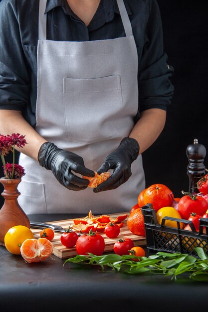 Cuoco femminile di vista frontale che pulisce i mandarini sul lavoro dell'alimento del pasto di verdure della dieta di salute dell'insalata di cottura scura