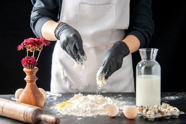 Cuoco femminile di vista frontale che rompe le uova in farina sul lavoro scuro pasticceria torta forno cottura torta pasta biscotto cuocere