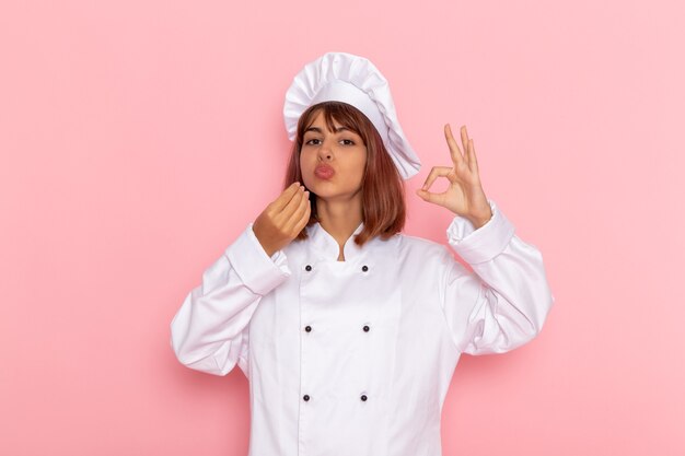 Cuoco femminile di vista frontale in vestito bianco del cuoco che posa su una superficie rosa