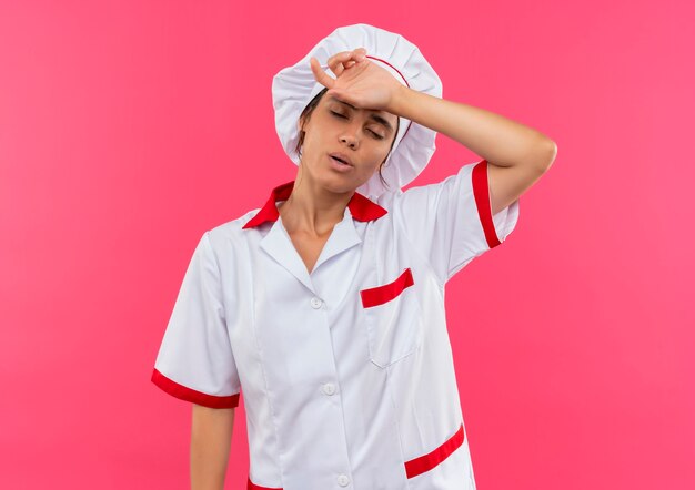 Cuoco femminile giovane stanco che indossa l'uniforme del cuoco unico che mette la mano sulla fronte con lo spazio della copia