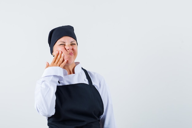 Cuoco femminile in uniforme, grembiule che soffre di mal di denti e dall'aspetto scomodo, vista frontale.