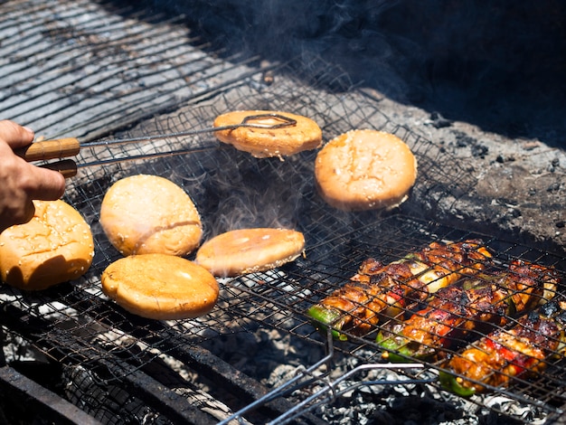 Cuoco irriconoscibile lanciando panini di hamburger che arrostiscono sulla griglia con le tenaglie