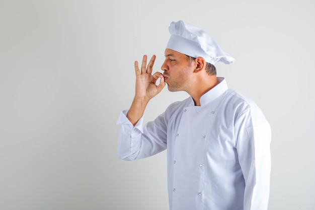 Cuoco maschio del cuoco unico che fa gesto saporito baciando le dita in cappello ed uniforme.
