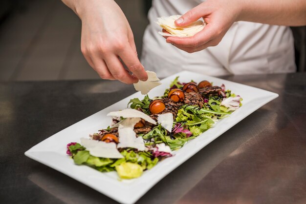 Cuoco unico che mette formaggio affettato su insalata