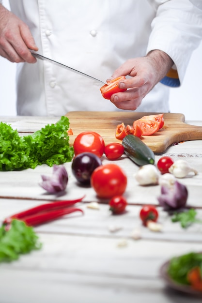 Cuoco unico che taglia un pomodoro rosso la sua cucina