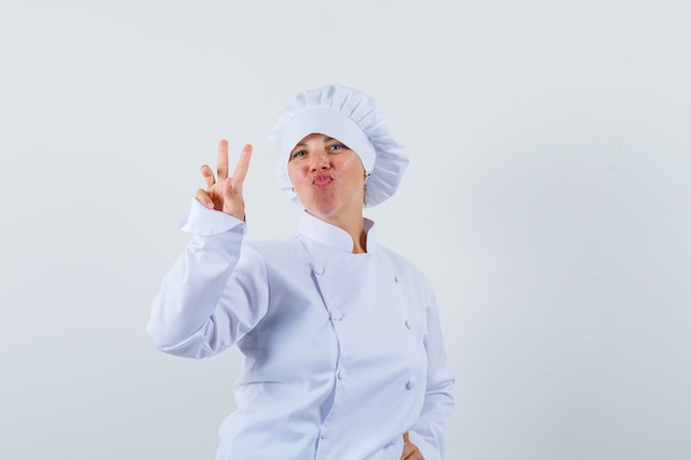 cuoco unico della donna che mostra il segno di V in uniforme bianca e che sembra fiducioso