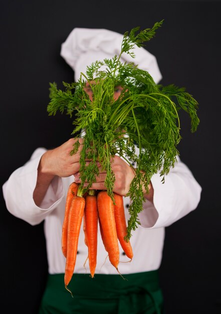 Cuoco unico di cucina che tiene mazzo di carote fresche