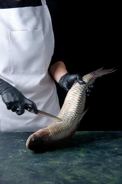 Cuoco unico di vista frontale in grembiule bianco che tiene pesce fresco e coltello sul tavolo