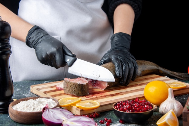 Cuoco unico di vista frontale in grembiule che taglia pesce crudo sul tagliere ciotola di farina sul tavolo da cucina