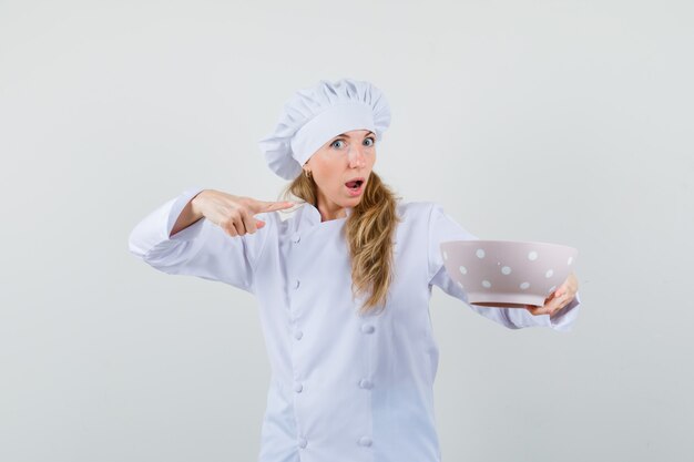 Cuoco unico femminile che indica alla ciotola in uniforme bianca e che sembra perplesso.