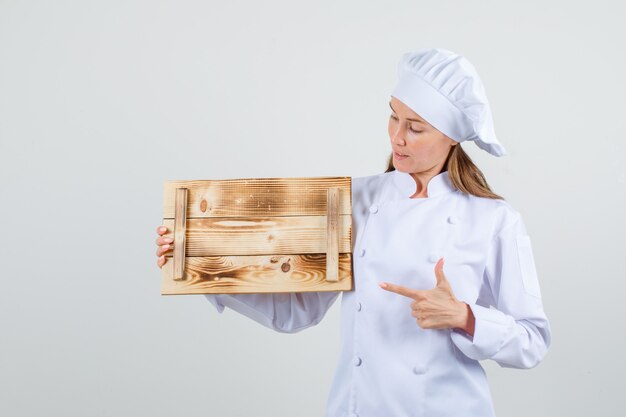 Cuoco unico femminile che indica il dito al vassoio di legno in uniforme bianca