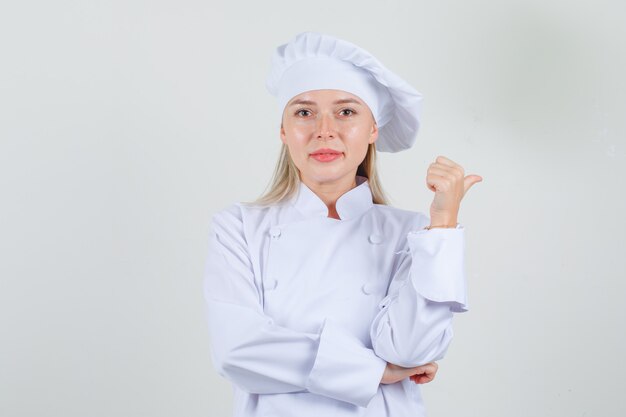 Cuoco unico femminile che indica il pollice a lato in uniforme bianca e che sembra allegro