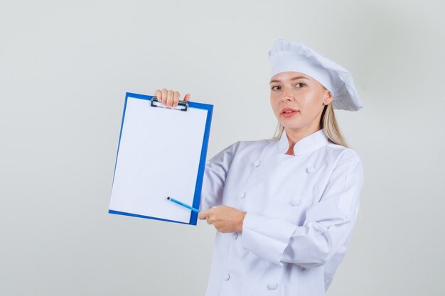 Cuoco unico femminile che indica matita negli appunti in uniforme bianca