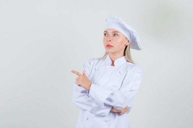 Cuoco unico femminile che indica via in uniforme bianca e che sembra premuroso. vista frontale.