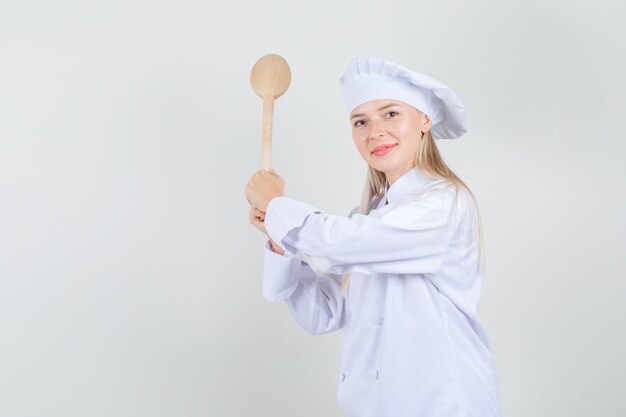 Cuoco unico femminile che minaccia con il cucchiaio di legno in uniforme bianca e che sembra allegro