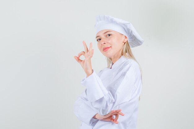 Cuoco unico femminile che mostra gesto giusto in uniforme bianca e che sembra allegro.