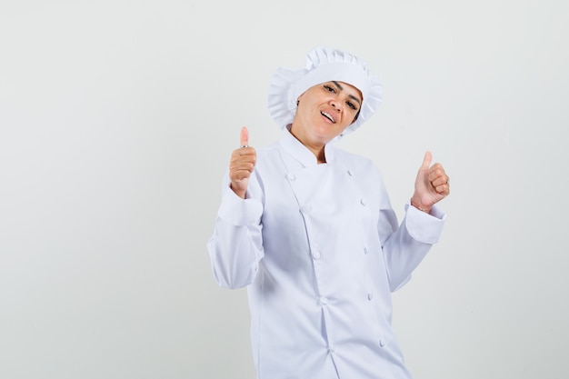 Cuoco unico femminile che mostra i doppi pollici in su in uniforme bianca e che sembra sicuro