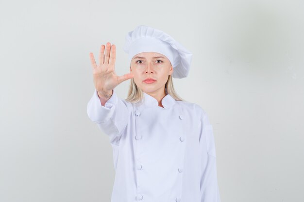 Cuoco unico femminile che mostra il gesto di arresto in uniforme bianca e che sembra serio