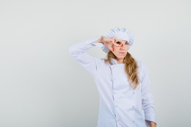 Cuoco unico femminile che osserva tramite le dita in uniforme bianca