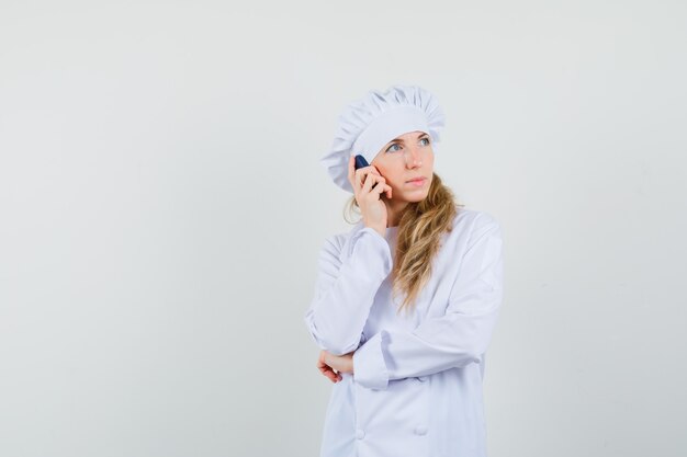 Cuoco unico femminile che parla sul telefono cellulare in uniforme bianca e che sembra pensieroso