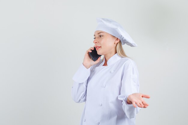 Cuoco unico femminile che parla sullo smartphone con il segno della mano in uniforme bianca