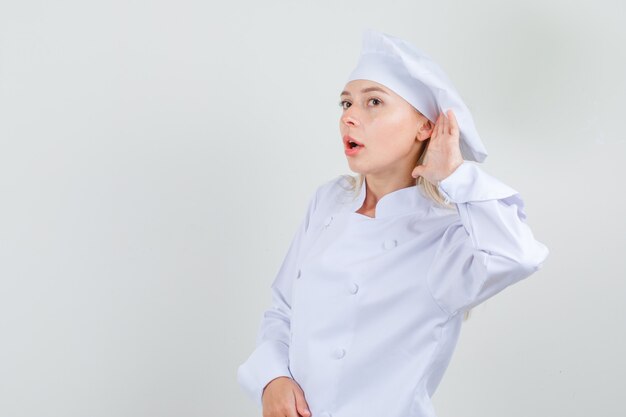 Cuoco unico femminile che prova a sentire qualcosa di riservato in uniforme bianca e che osserva cauto.