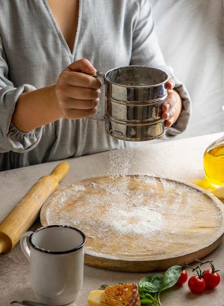 Cuoco unico femminile che setaccia la farina sopra il bordo di legno per rotolare la pasta della pizza