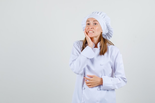 Cuoco unico femminile che soffre di mal di denti in uniforme bianca e sembra doloroso