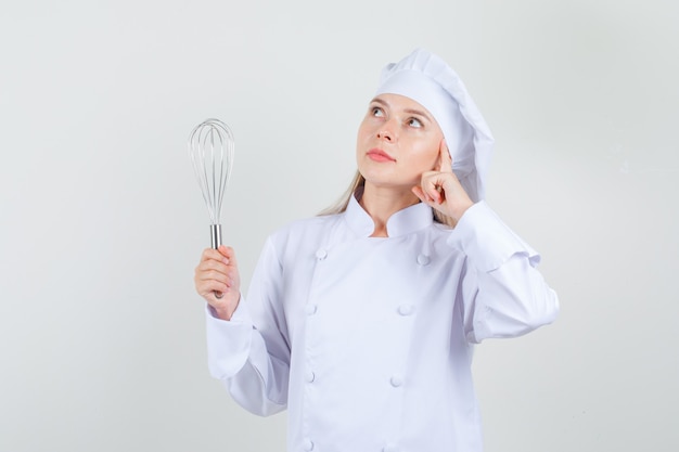 Cuoco unico femminile che tiene frusta e che osserva in su sognante in uniforme bianca