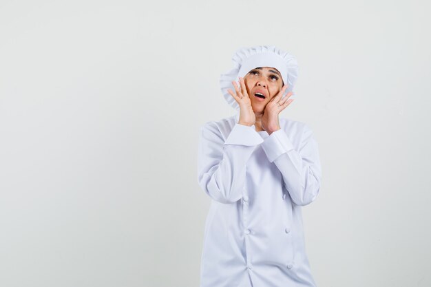 Cuoco unico femminile che tiene le mani vicino alla bocca in uniforme bianca e che sembra preoccupato