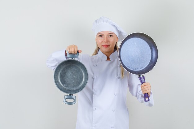 Cuoco unico femminile che tiene pentole vuote e sorridente in uniforme bianca