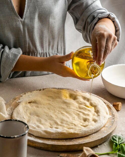 Cuoco unico femminile che versa l'olio sopra la pasta della pizza